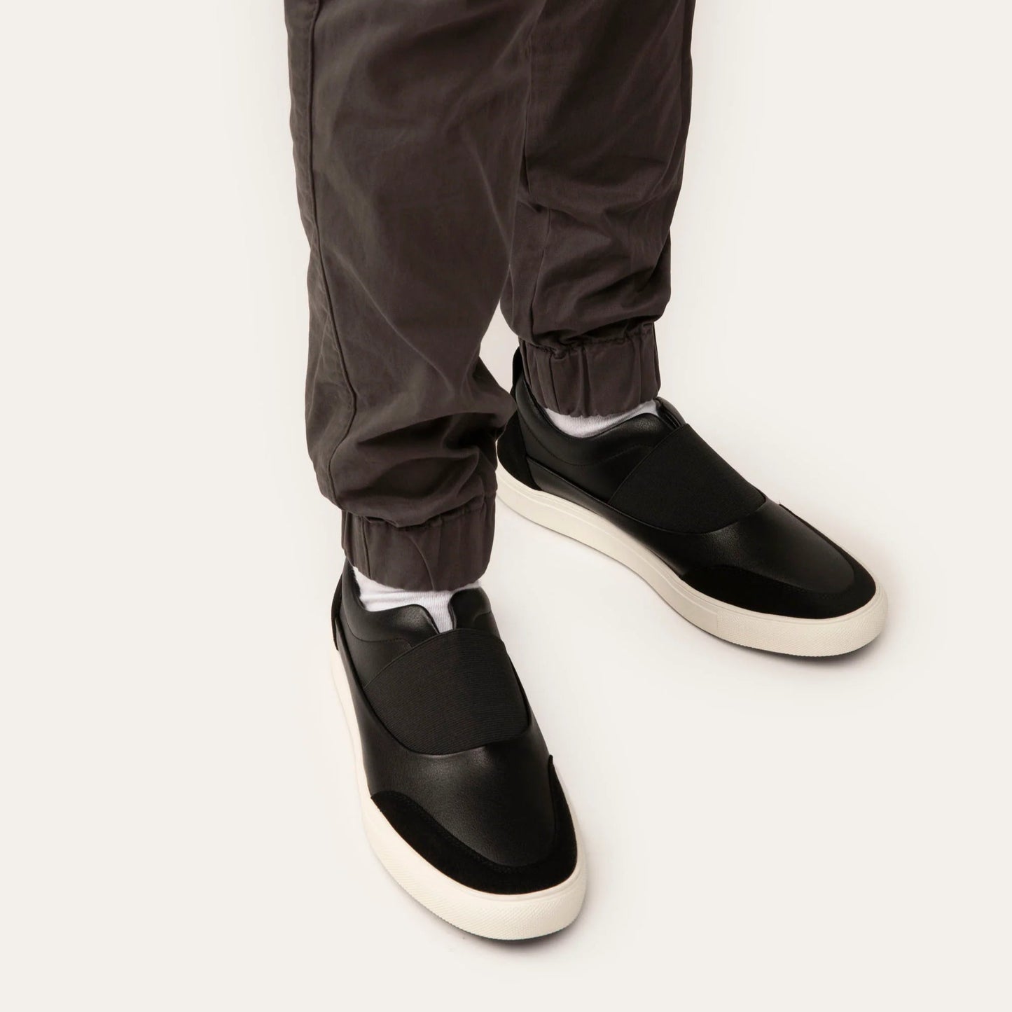 Black slip-on shoes worn with dark pants on a white background