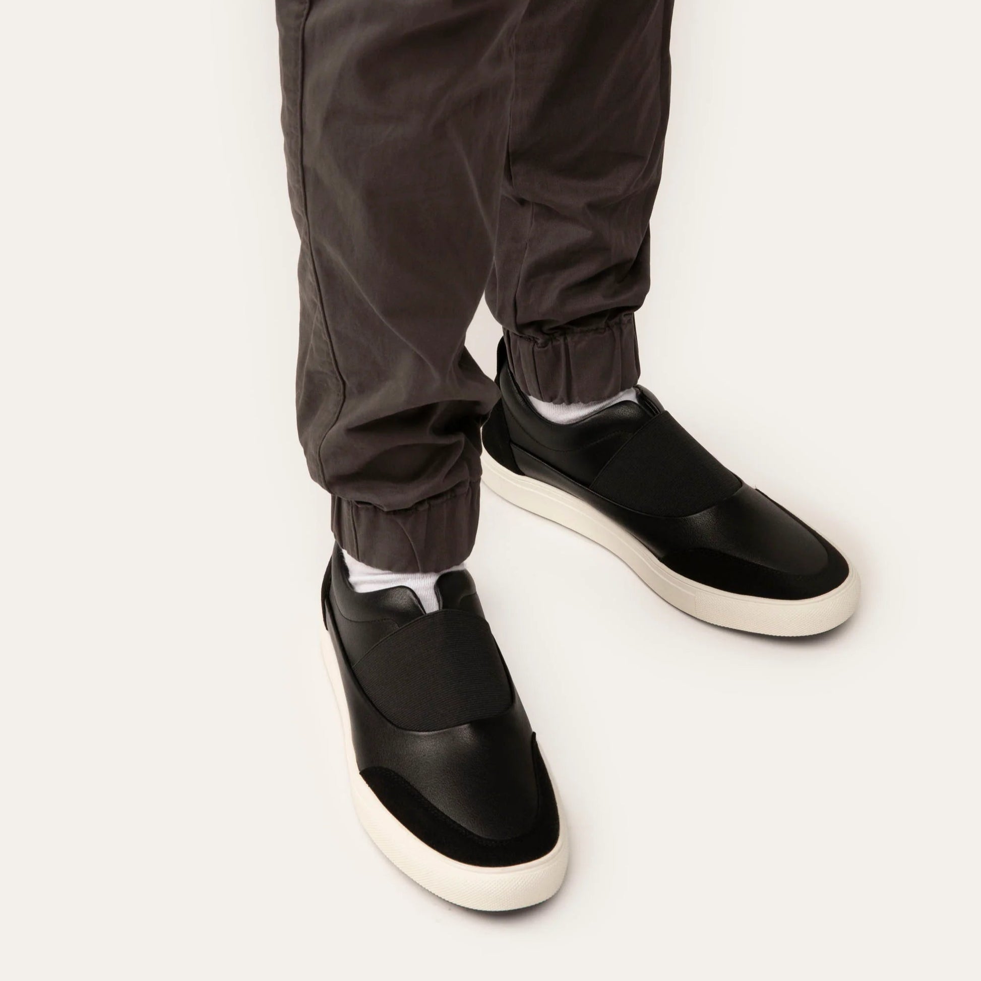 Black slip-on shoes worn with dark pants on a white background
